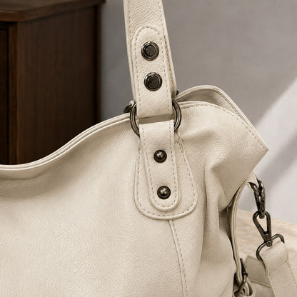 Tæt på nittebesatte håndtagstapper på creme hobo bag